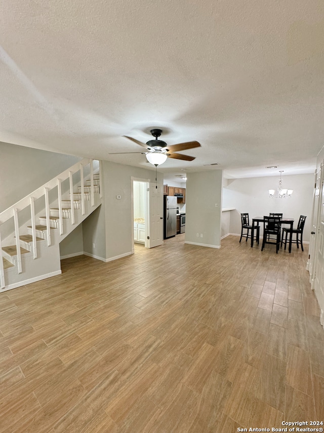 unfurnished living room featuring a textured ceiling, light hardwood / wood-style floors, and ceiling fan with notable chandelier