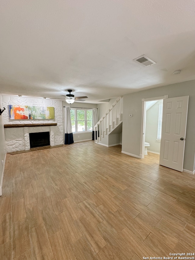 unfurnished living room featuring ceiling fan, light hardwood / wood-style floors, and a stone fireplace