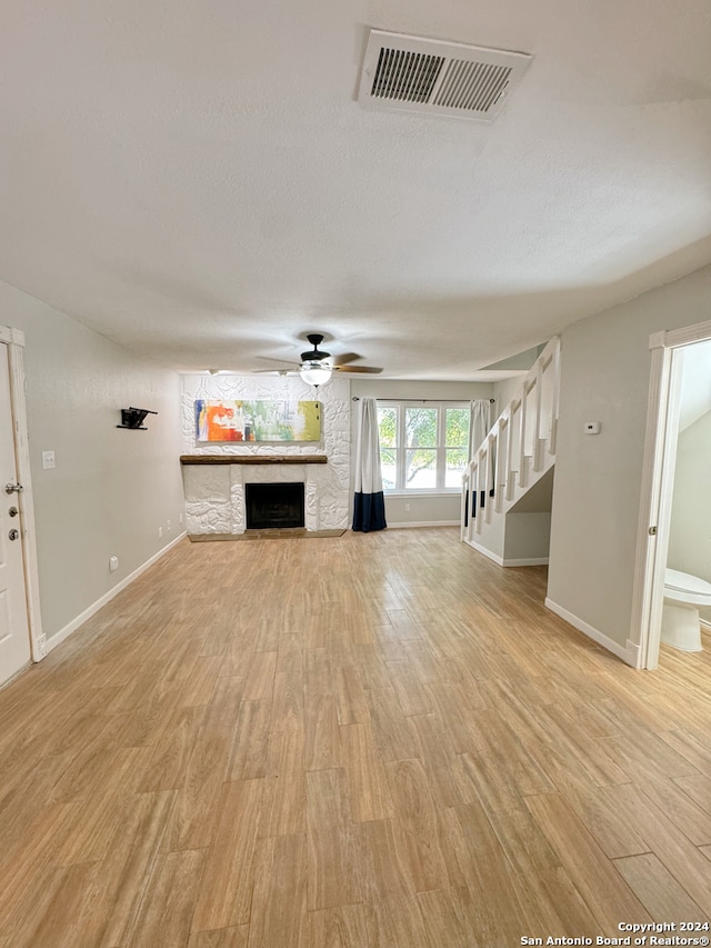 unfurnished living room with light wood-type flooring, a stone fireplace, and ceiling fan