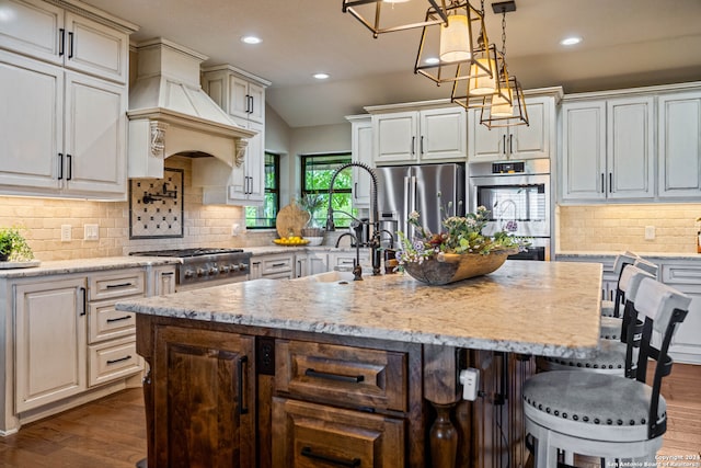 kitchen with hardwood / wood-style floors, appliances with stainless steel finishes, tasteful backsplash, and an island with sink