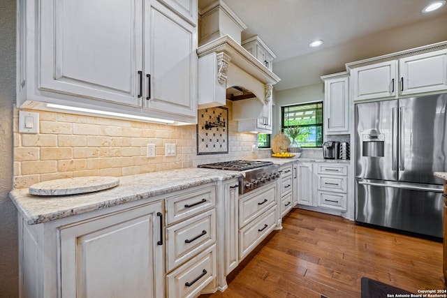 kitchen featuring light stone countertops, white cabinetry, wood finished floors, stainless steel appliances, and decorative backsplash