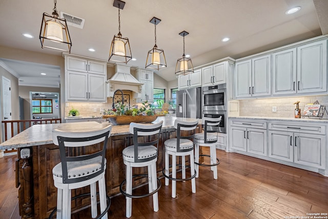 kitchen featuring appliances with stainless steel finishes, decorative light fixtures, decorative backsplash, a kitchen island, and dark wood-type flooring