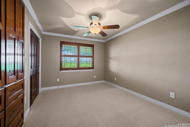 spare room featuring a textured ceiling, ornamental molding, a ceiling fan, light carpet, and baseboards
