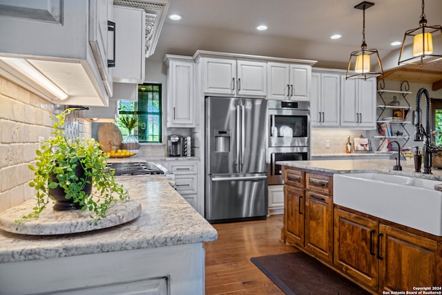 kitchen featuring wood-type flooring, stainless steel appliances, tasteful backsplash, hanging light fixtures, and white cabinets