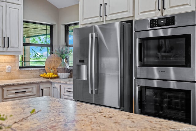 kitchen featuring stainless steel appliances, light stone countertops, white cabinetry, and tasteful backsplash