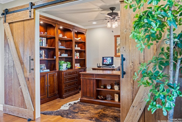 office space with ceiling fan, a barn door, crown molding, and hardwood / wood-style flooring