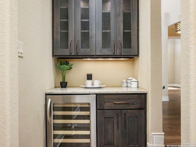 bar featuring light stone countertops, dark brown cabinetry, beverage cooler, and hardwood / wood-style floors