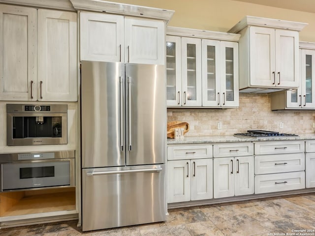 kitchen with tasteful backsplash, appliances with stainless steel finishes, light stone counters, and light tile patterned floors