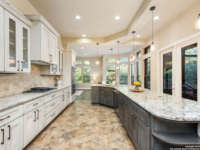 kitchen with backsplash, stainless steel appliances, a spacious island, light stone countertops, and white cabinets