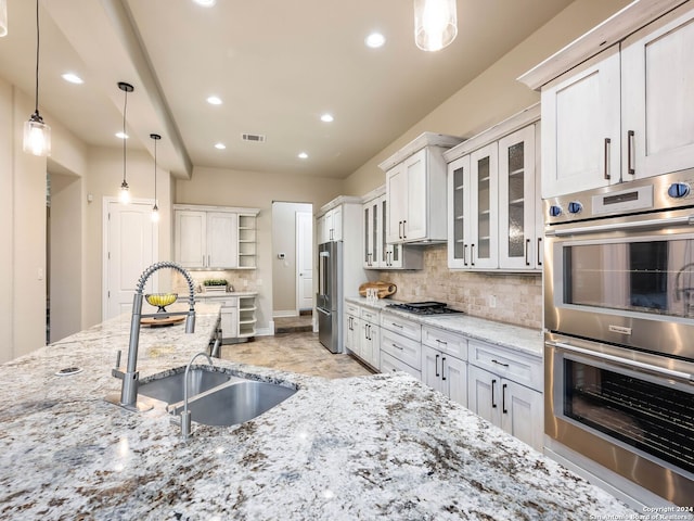 kitchen featuring tasteful backsplash, light stone counters, sink, decorative light fixtures, and stainless steel appliances