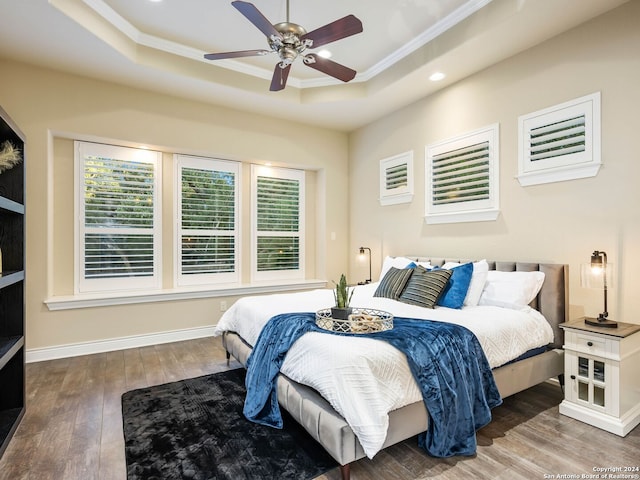 bedroom with ceiling fan, a tray ceiling, hardwood / wood-style floors, and ornamental molding