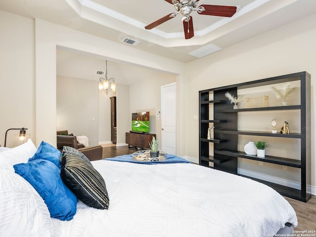 bedroom featuring ceiling fan with notable chandelier, a raised ceiling, and hardwood / wood-style flooring