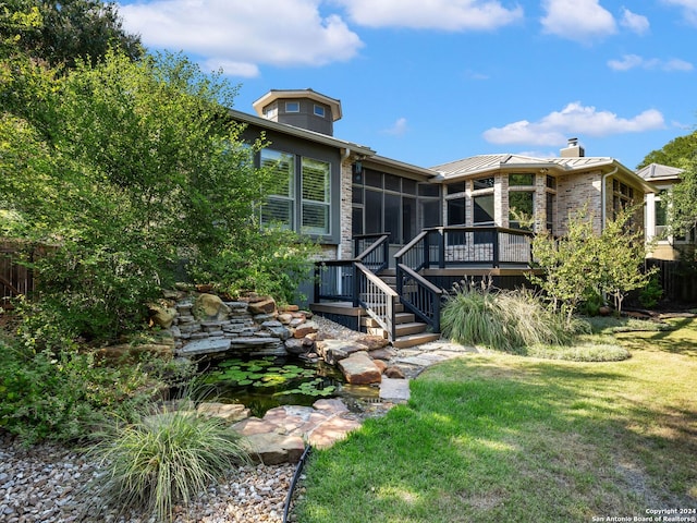 rear view of property with a sunroom, a wooden deck, and a lawn