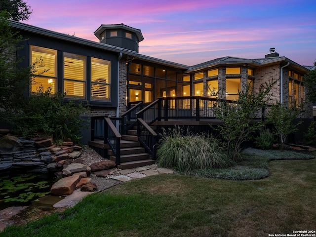 back house at dusk featuring a wooden deck and a yard