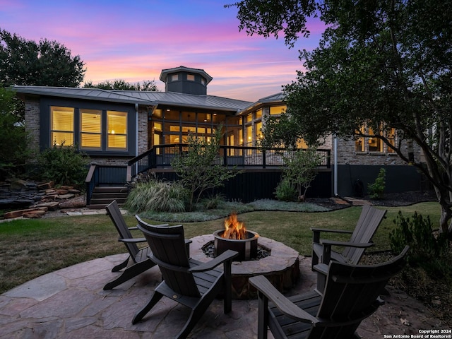 back house at dusk featuring a lawn, an outdoor fire pit, and a patio area