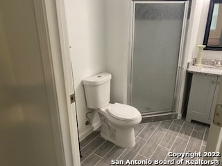 bathroom featuring a shower with door, toilet, and vanity