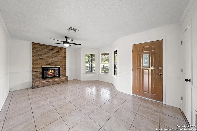 tiled entrance foyer with ceiling fan, crown molding, a textured ceiling, and a brick fireplace