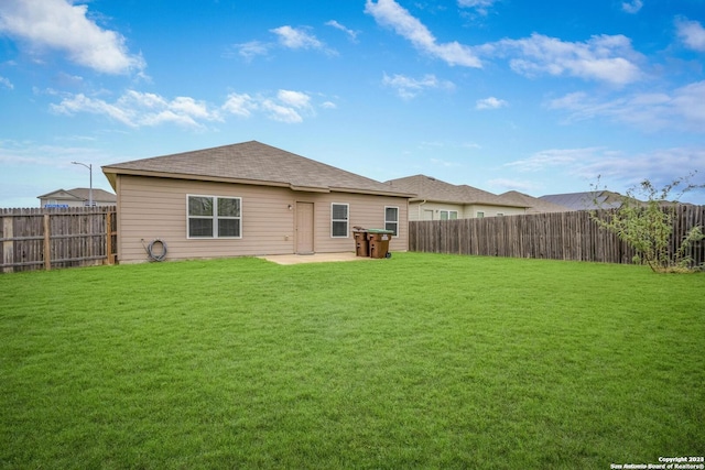 rear view of property featuring a patio area, a fenced backyard, a yard, and roof with shingles