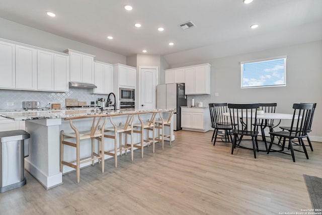 kitchen with light hardwood / wood-style flooring, light stone counters, decorative backsplash, stainless steel appliances, and white cabinets