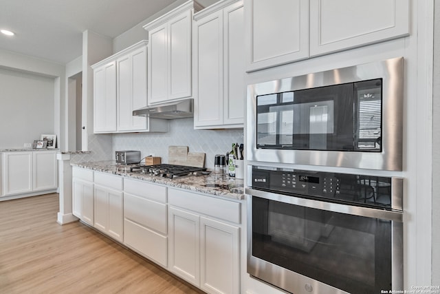 kitchen with light wood-type flooring, decorative backsplash, wall chimney exhaust hood, white cabinets, and stainless steel appliances