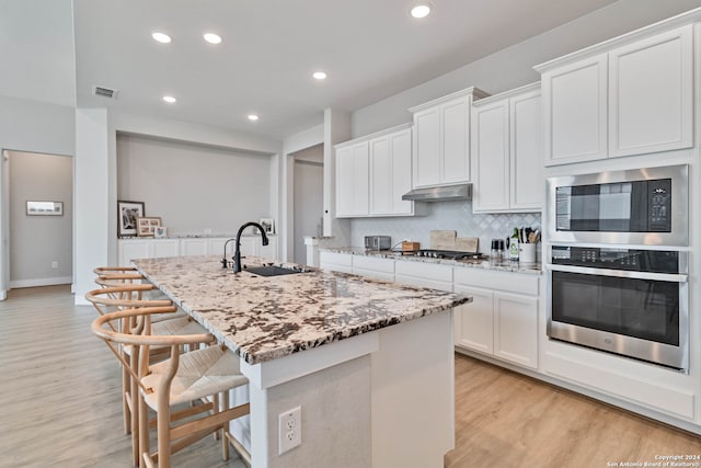 kitchen with sink, appliances with stainless steel finishes, decorative backsplash, light hardwood / wood-style floors, and a center island with sink