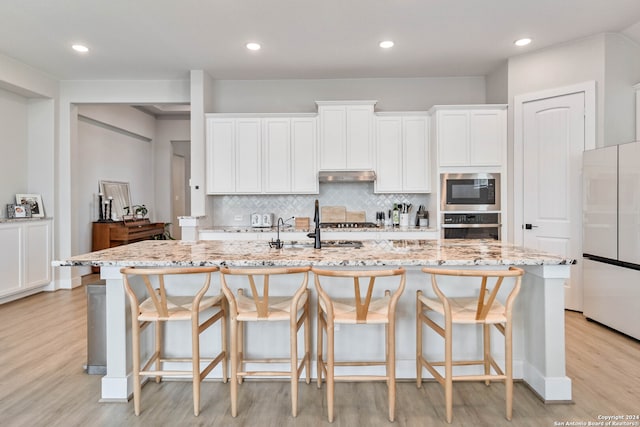 kitchen with a kitchen island with sink, backsplash, light hardwood / wood-style flooring, and appliances with stainless steel finishes