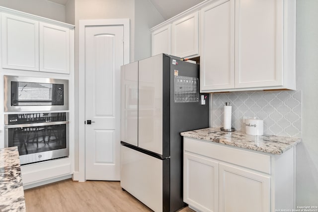 kitchen featuring light wood-type flooring, backsplash, white cabinets, appliances with stainless steel finishes, and light stone countertops