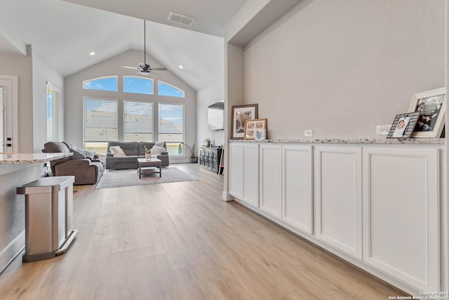 interior space featuring ceiling fan, high vaulted ceiling, white cabinetry, light hardwood / wood-style floors, and light stone countertops