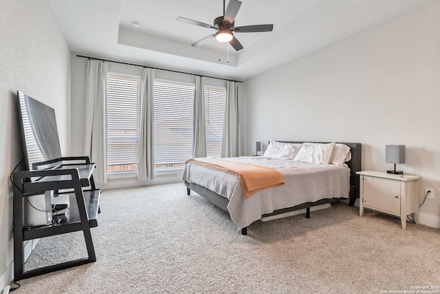 carpeted bedroom featuring multiple windows, a tray ceiling, and ceiling fan