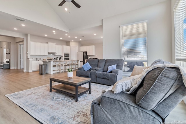 living room with light wood-type flooring, high vaulted ceiling, sink, and ceiling fan