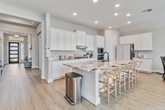 kitchen with appliances with stainless steel finishes, a center island with sink, light hardwood / wood-style floors, and tasteful backsplash