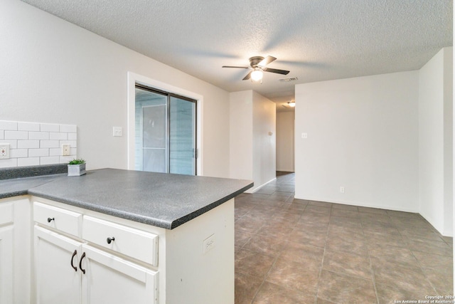 kitchen with white cabinets, dark countertops, ceiling fan, a peninsula, and backsplash