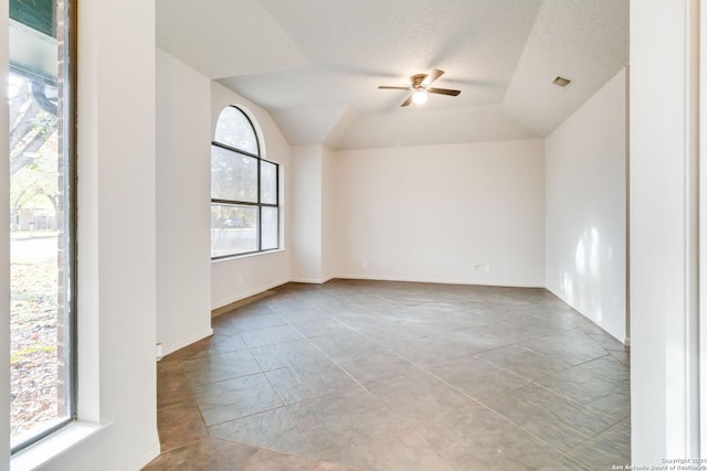 empty room featuring baseboards, visible vents, a ceiling fan, vaulted ceiling, and a textured ceiling