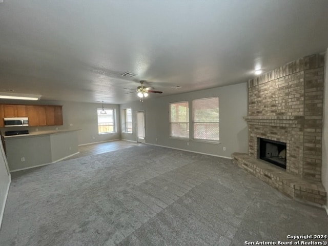 unfurnished living room with ceiling fan, a fireplace, brick wall, and carpet flooring