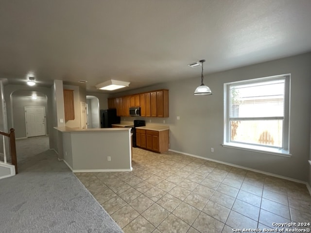 kitchen with decorative light fixtures, stove, light carpet, kitchen peninsula, and refrigerator