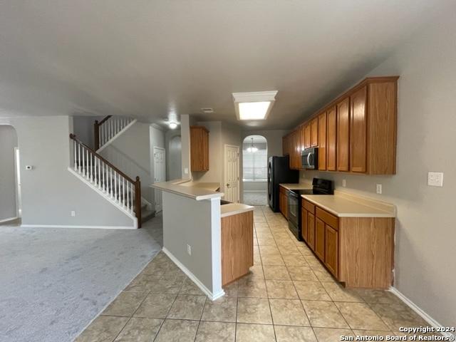 kitchen with kitchen peninsula, black appliances, and light colored carpet