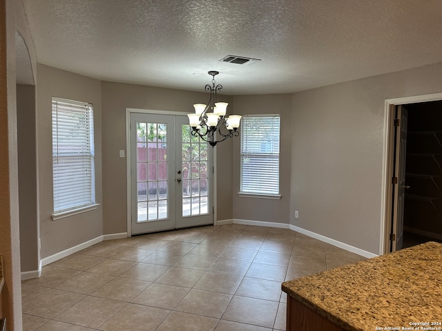 unfurnished dining area featuring a textured ceiling, french doors, light tile patterned flooring, and a chandelier