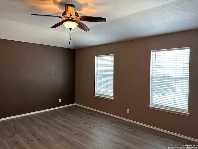 empty room featuring ceiling fan, plenty of natural light, a textured ceiling, and dark wood-type flooring