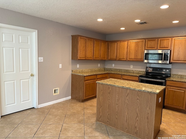 kitchen featuring a kitchen island, appliances with stainless steel finishes, light stone countertops, a textured ceiling, and light tile patterned flooring