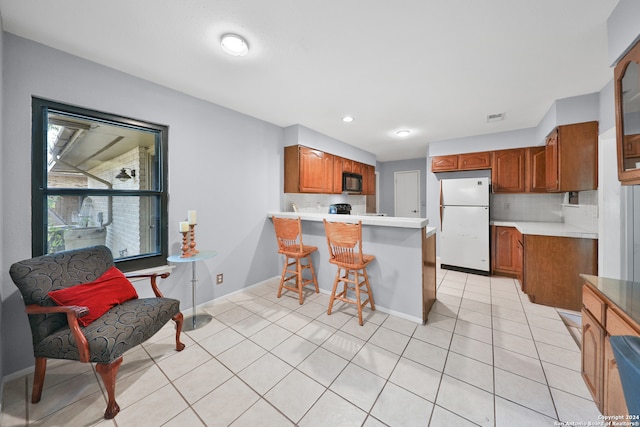 kitchen with light tile patterned floors, kitchen peninsula, white fridge, and tasteful backsplash