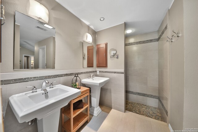 bathroom with backsplash, dual sinks, a tile shower, tile walls, and ceiling fan