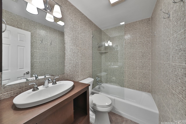 full bathroom with tile walls, tiled shower / bath, vanity, and toilet