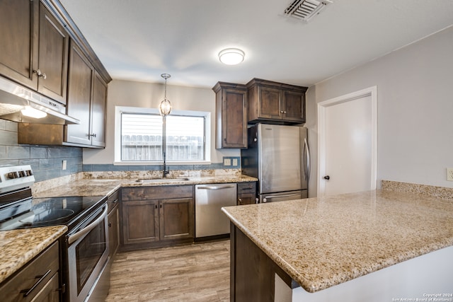 kitchen with sink, light wood-type flooring, appliances with stainless steel finishes, light stone counters, and tasteful backsplash