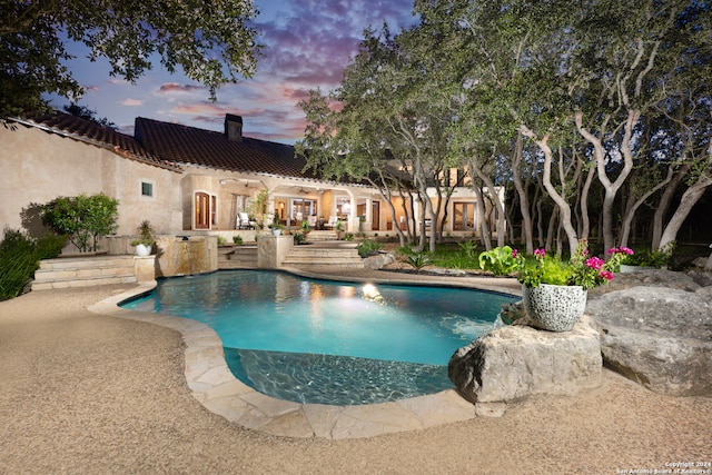 pool at dusk with a patio and pool water feature