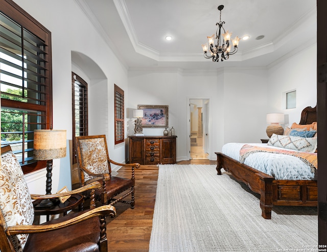 bedroom featuring a notable chandelier, ensuite bathroom, wood-type flooring, a tray ceiling, and crown molding