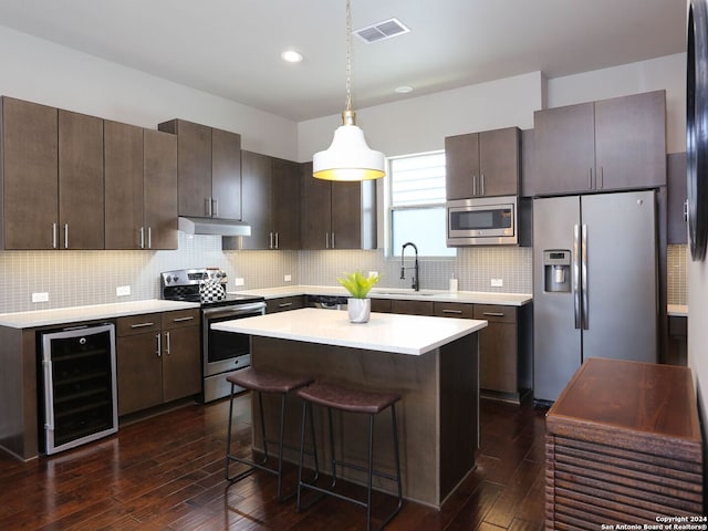 kitchen featuring a kitchen island, wine cooler, hanging light fixtures, stainless steel appliances, and decorative backsplash