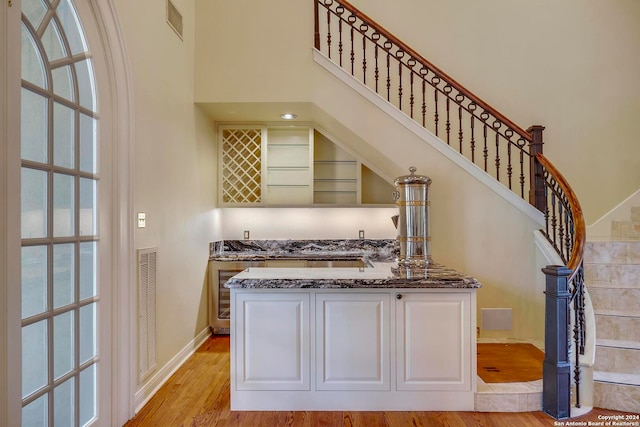 kitchen with a high ceiling, dark stone countertops, white cabinets, and light hardwood / wood-style floors