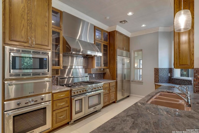 kitchen featuring wall chimney exhaust hood, built in appliances, sink, and decorative backsplash