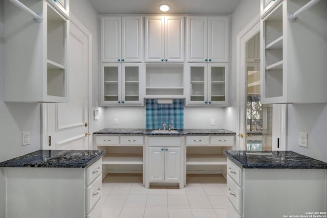 kitchen featuring dark stone countertops, white cabinetry, light tile patterned floors, and sink