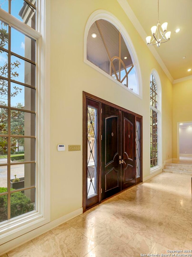 entryway with ornamental molding, a towering ceiling, plenty of natural light, and an inviting chandelier